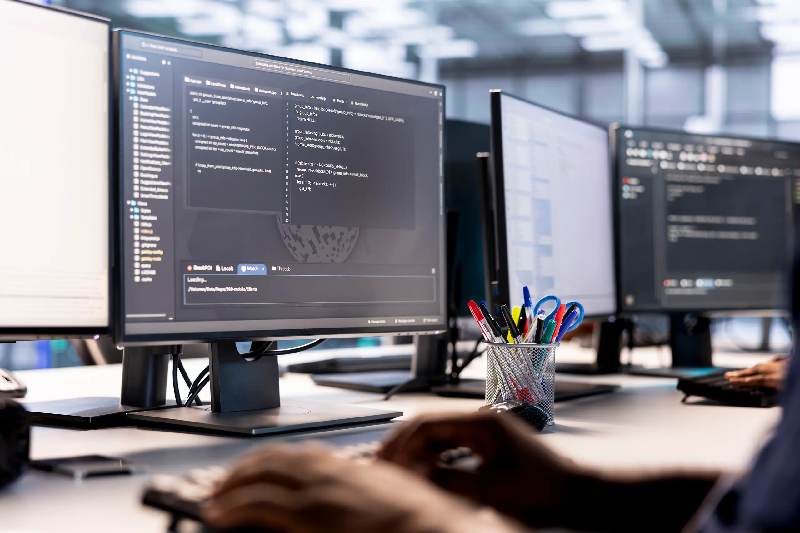 Dual monitor close-up with code, person typing in a data center