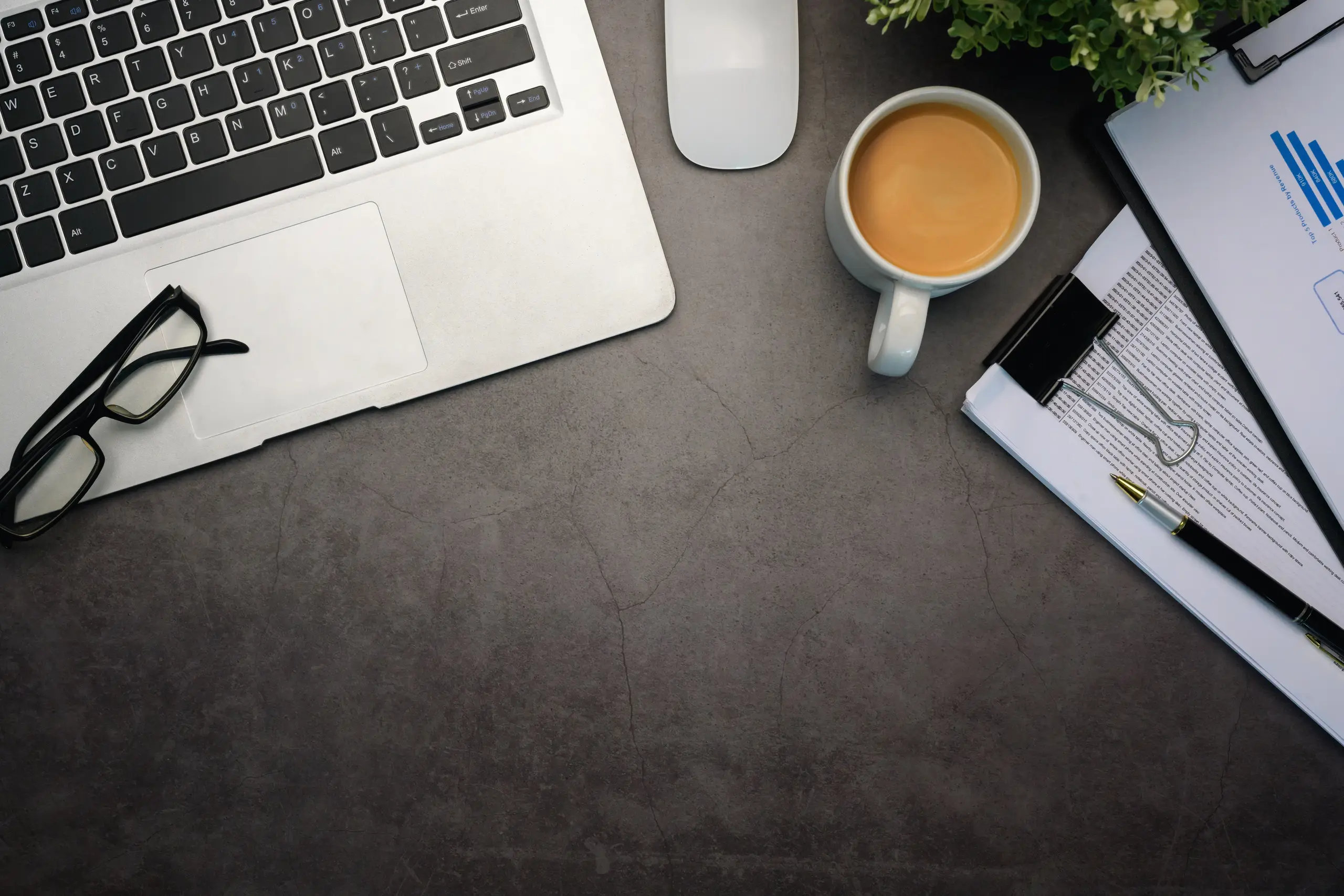 Flat lay of laptop, coffee and financial reports on a dark stone surface