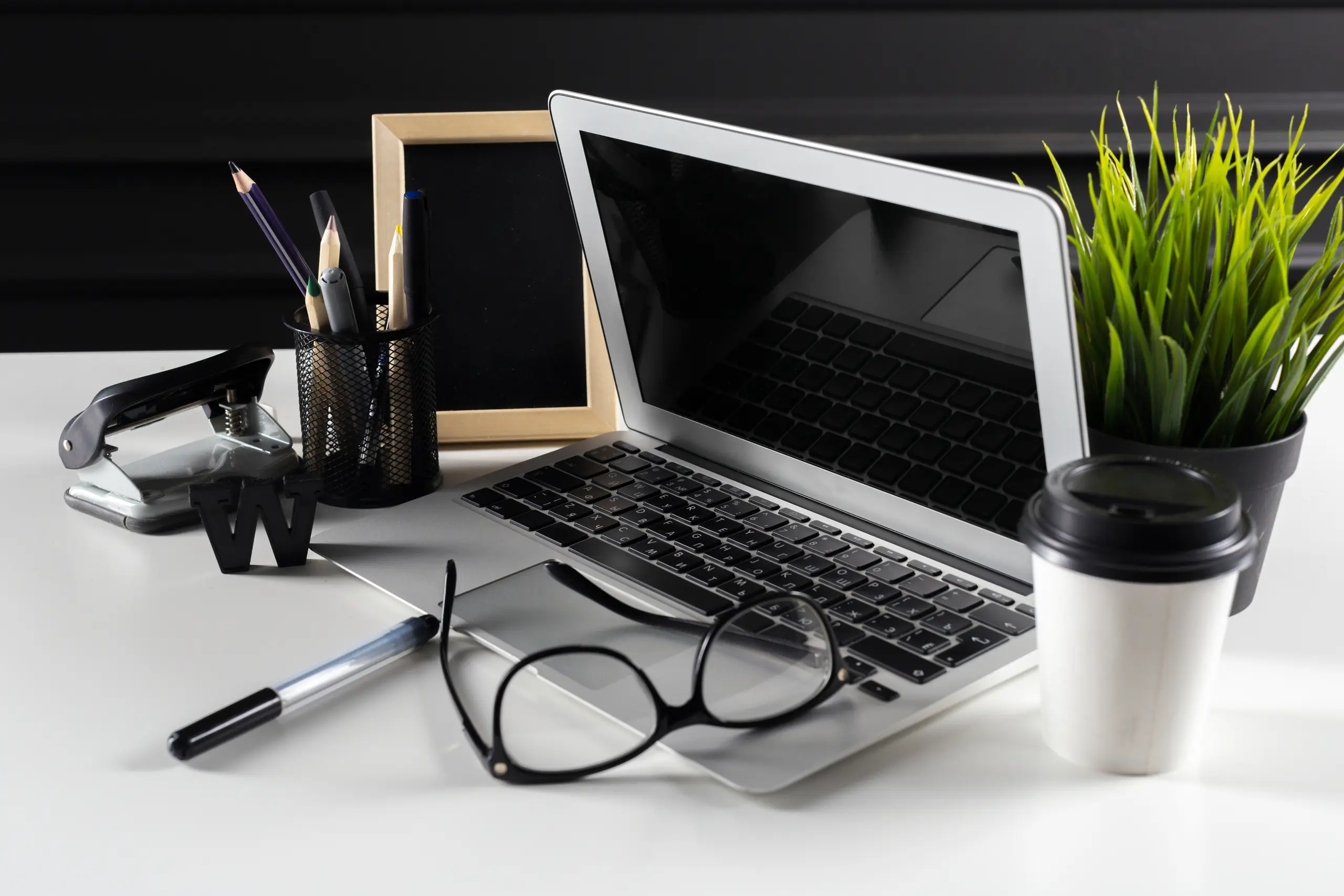 Laptop with glasses, plant, pens and coffee, angled view