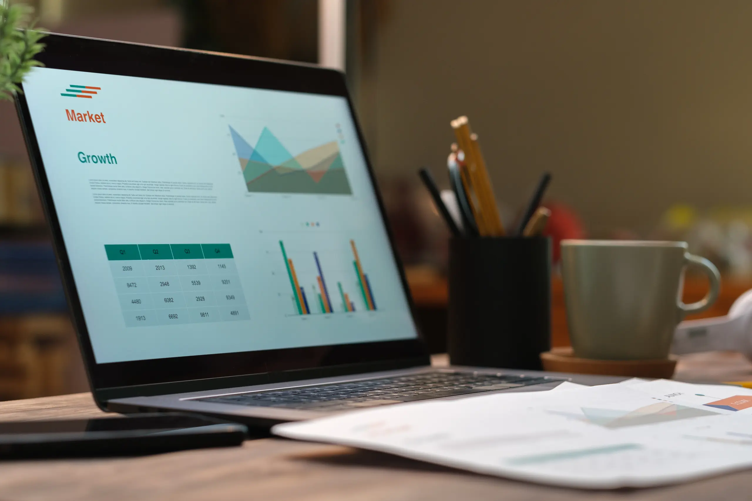 Laptop showing market growth chart with coffee and pen