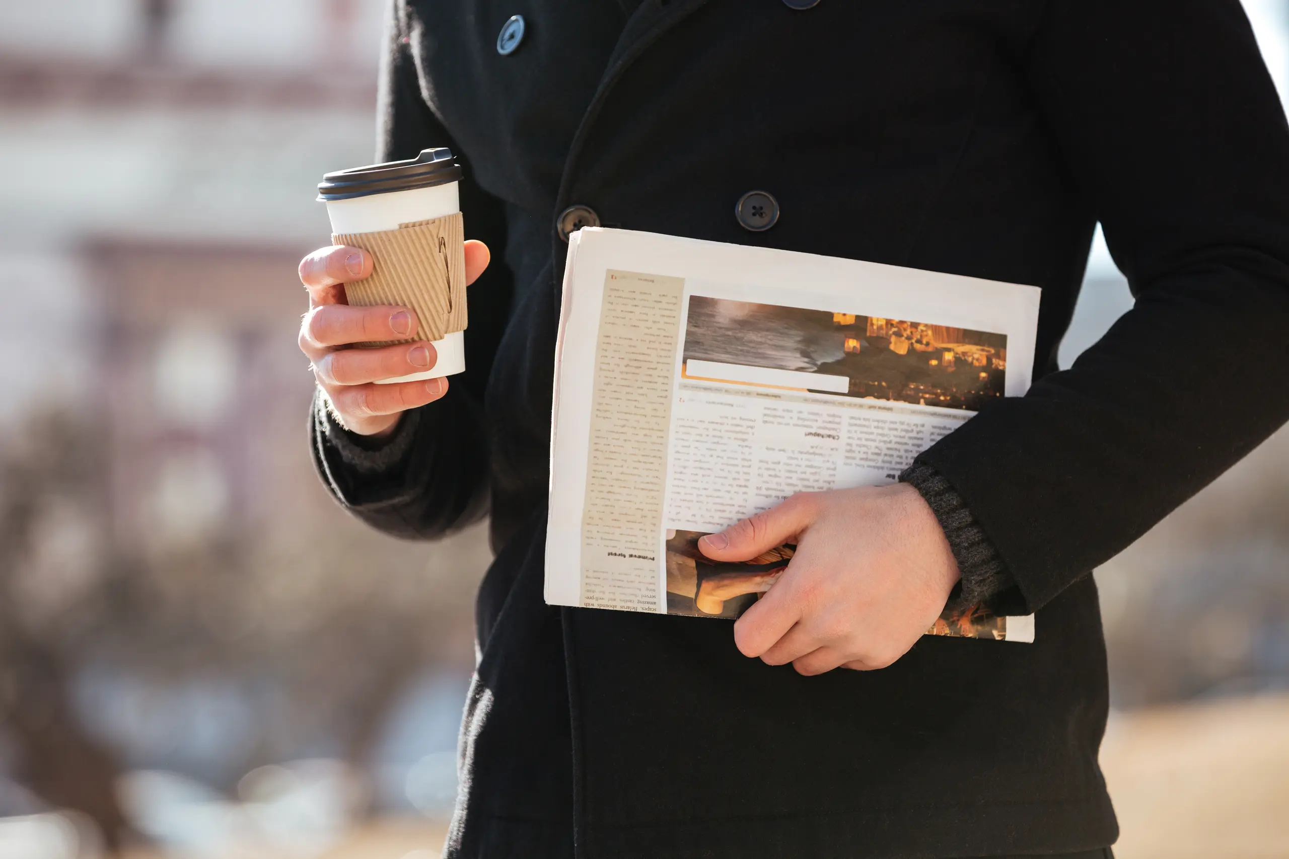 Man walking in a city with coffee and a newspaper