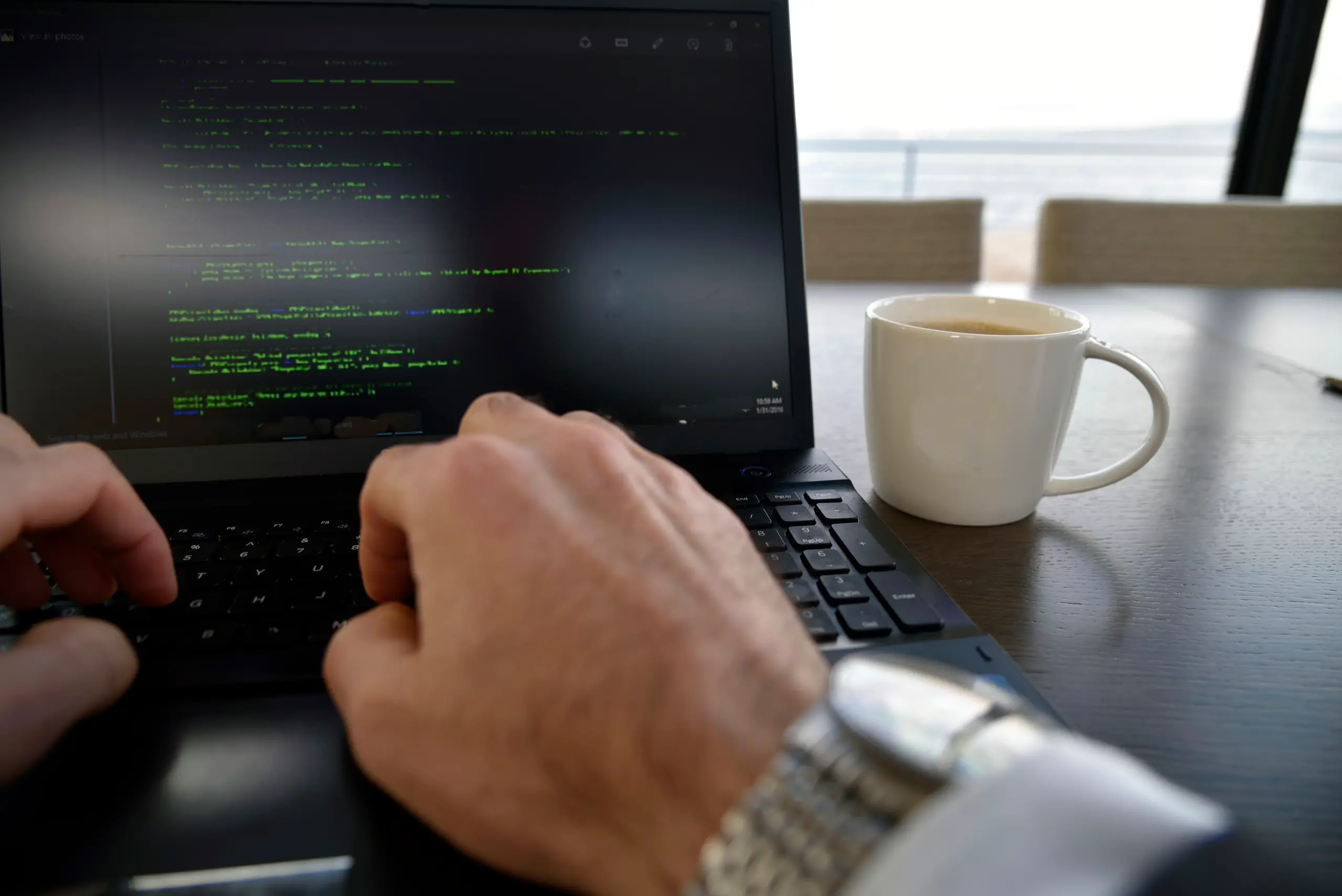 Person typing code on a laptop with coffee