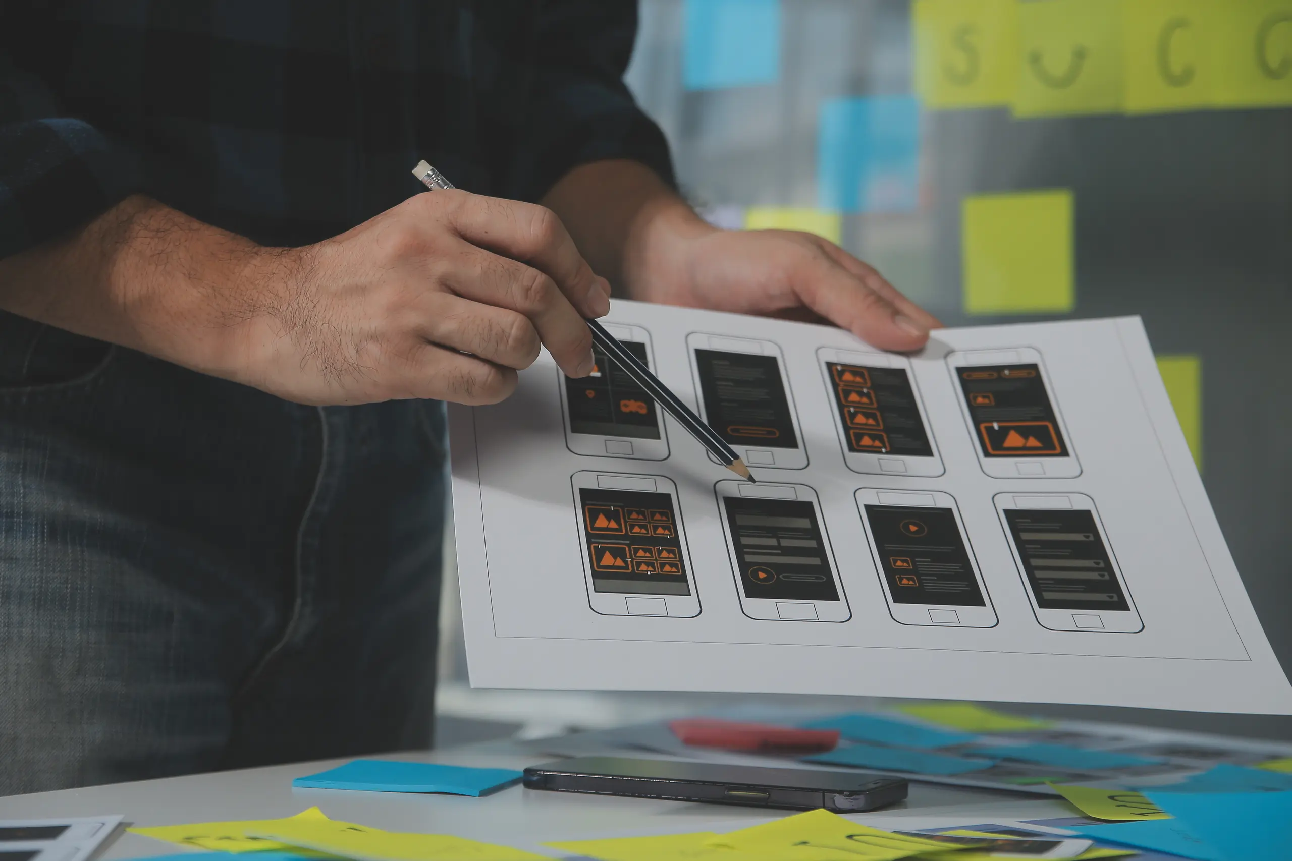Person holding phone UI/UX design sheet and pointing with pen