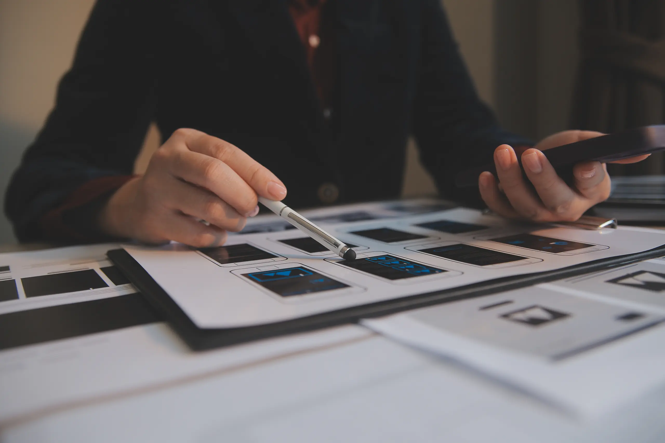 Person pointing at phone UI/UX design with a pen, front view
