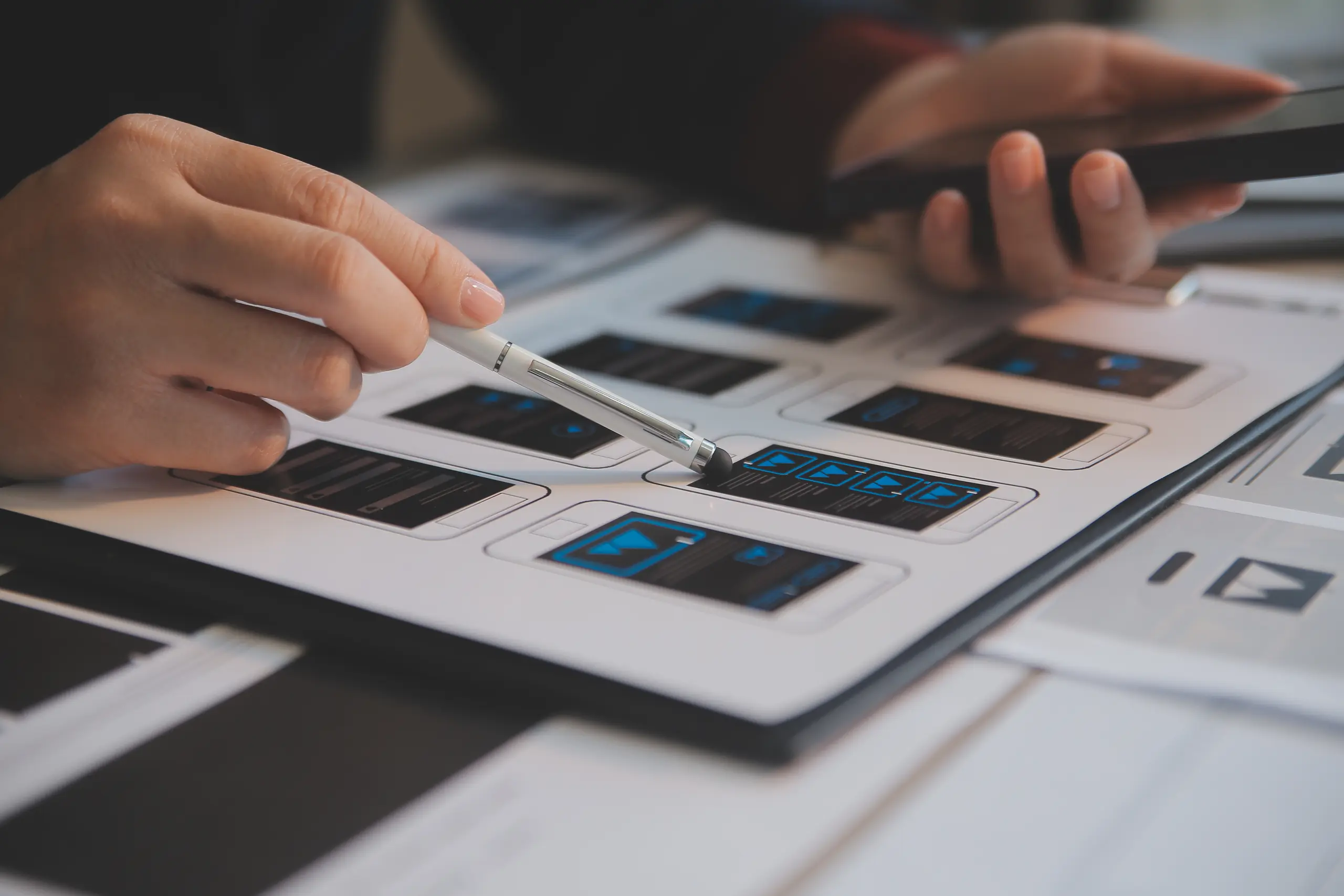 Person pointing at phone UI/UX design with a pen, side view