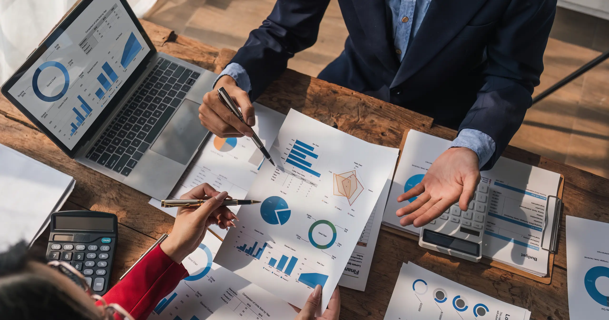 Two people discussing data sheets with a laptop and calculator
