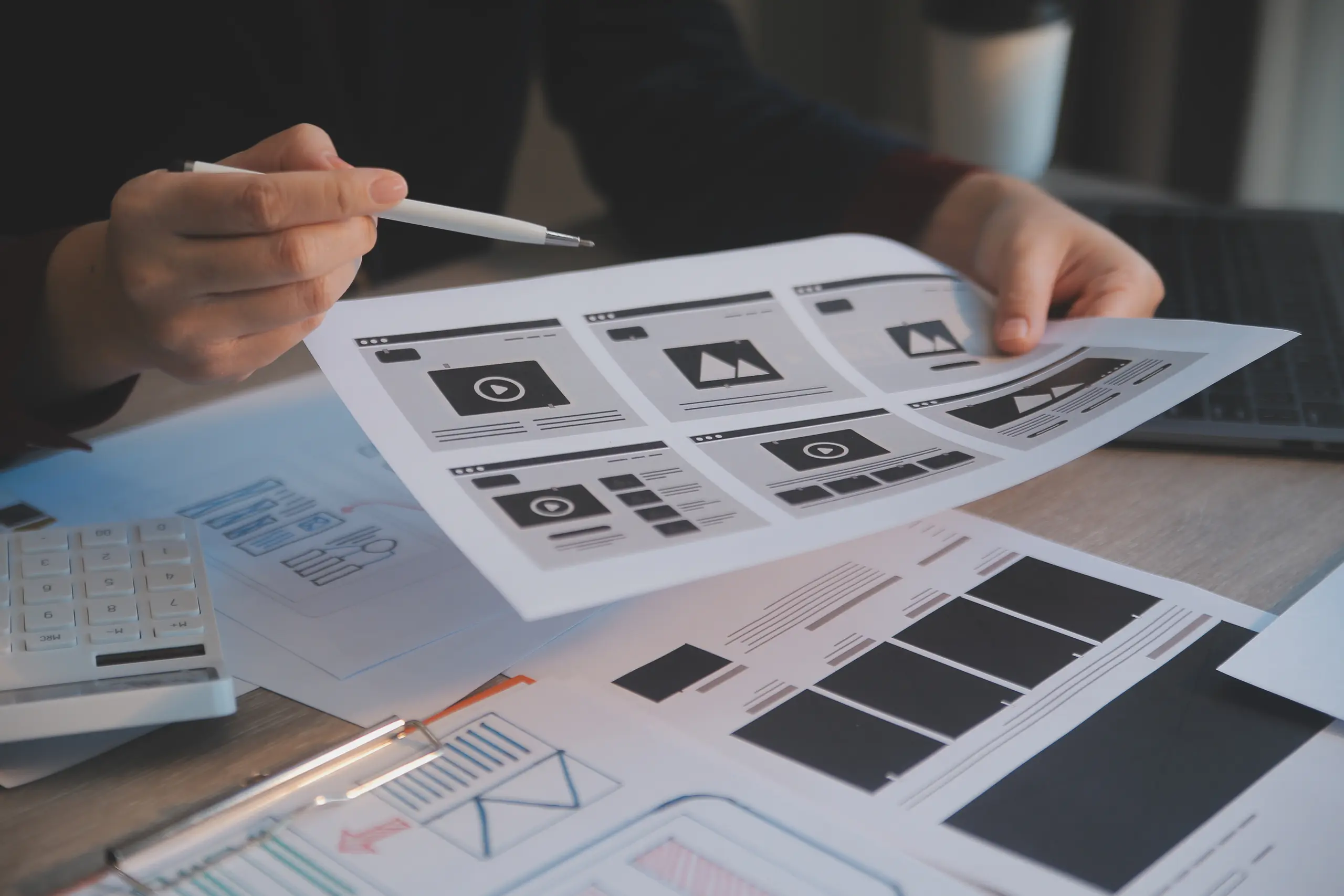 Person pointing at website UI/UX design sheets with a pen